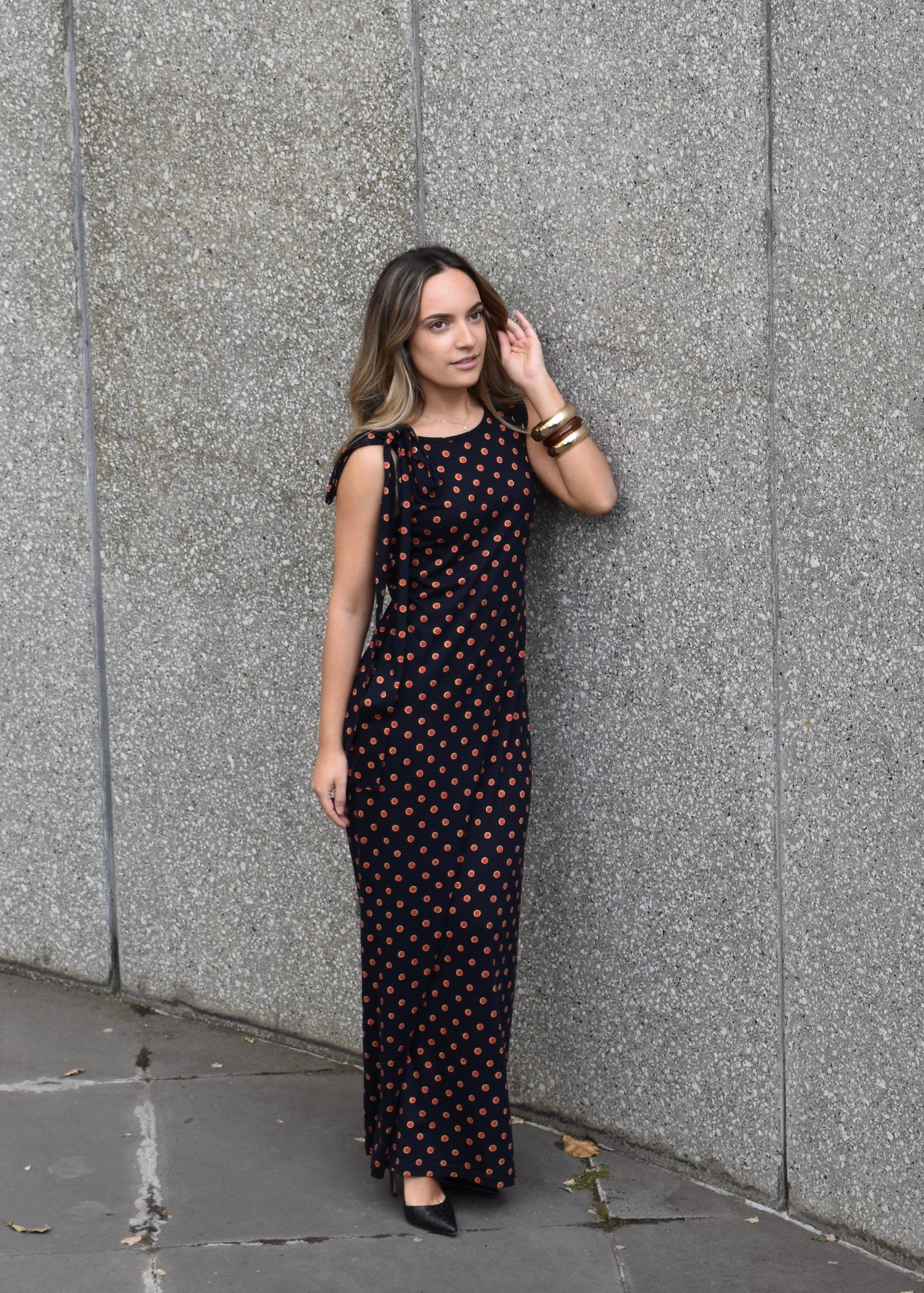 Woman in a Missou polka dot dress standing against a gray wall.