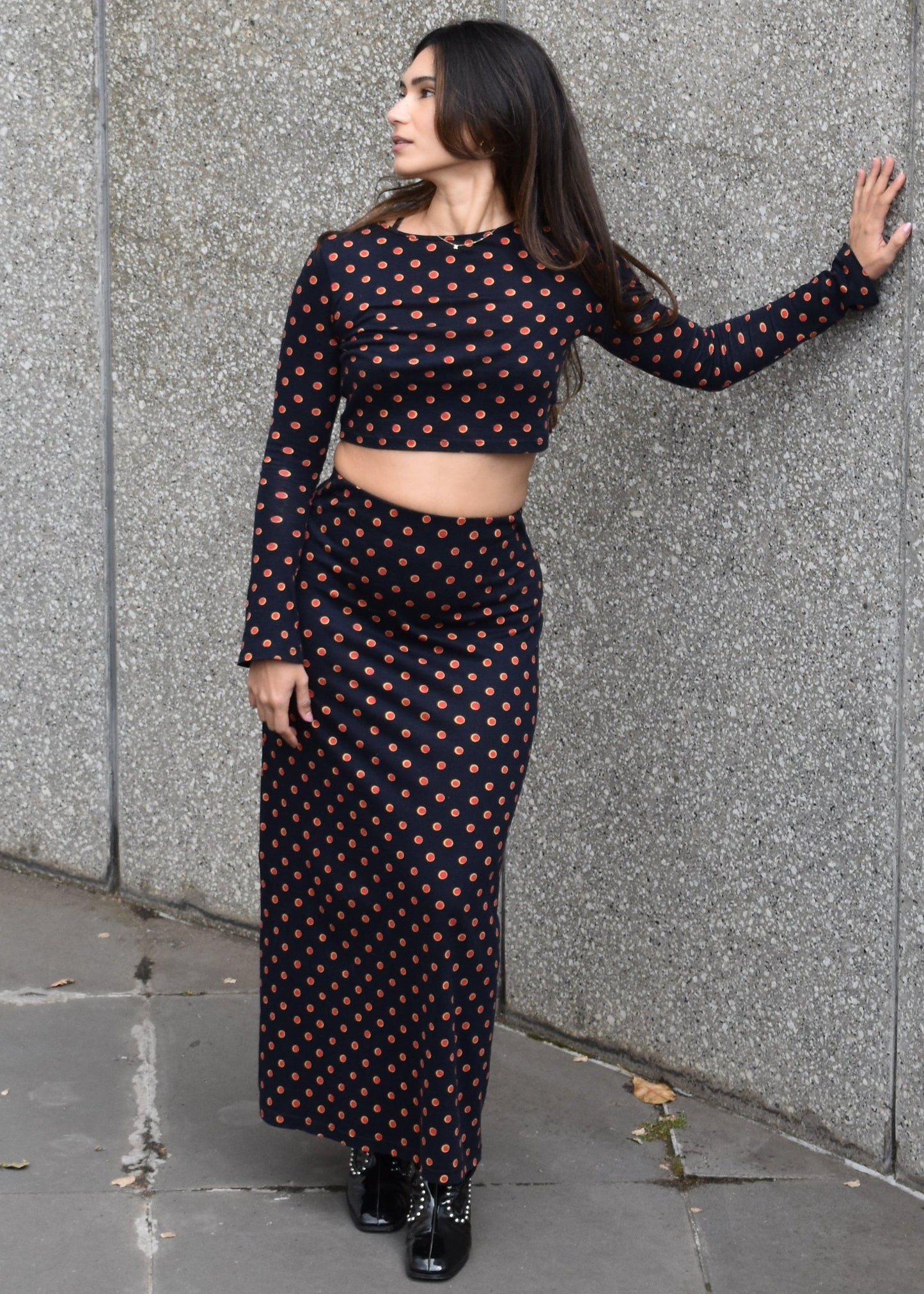 Woman facing front wearing the Isabel maxi skirt high waisted and matching Tati flared long sleeve cropped top in navy Japanese Tashi Spot print in front of a stone wall. Australian made.