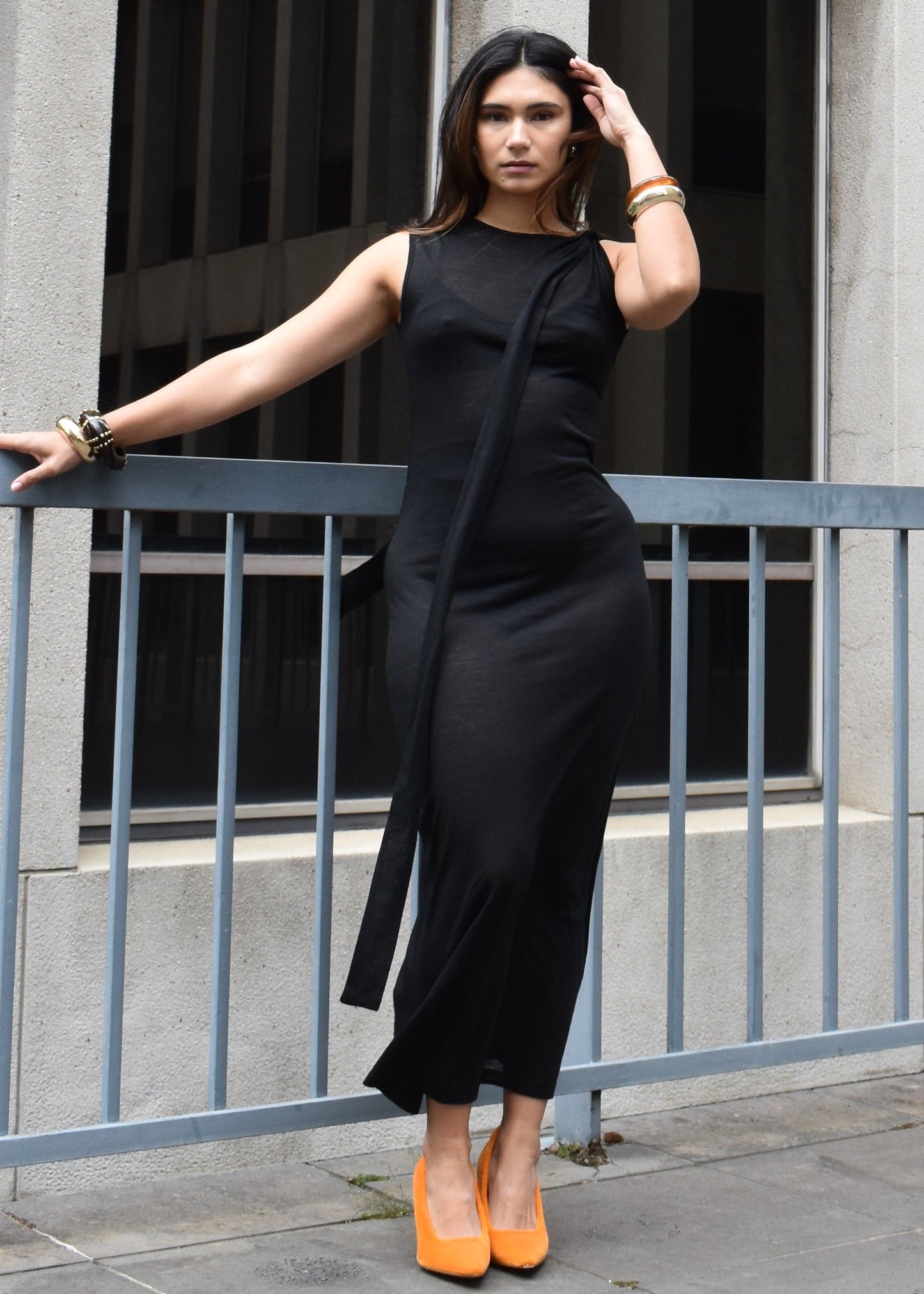 Woman in a black sheer japanese tencel merino blend dress with orange shoes standing on a city street.