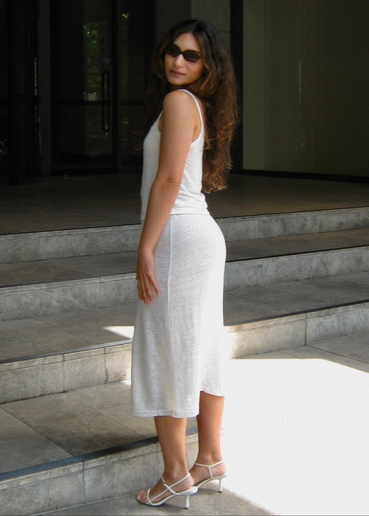Woman in a white Japanese linen cami top and midi skirt standing on steps outside a modern building