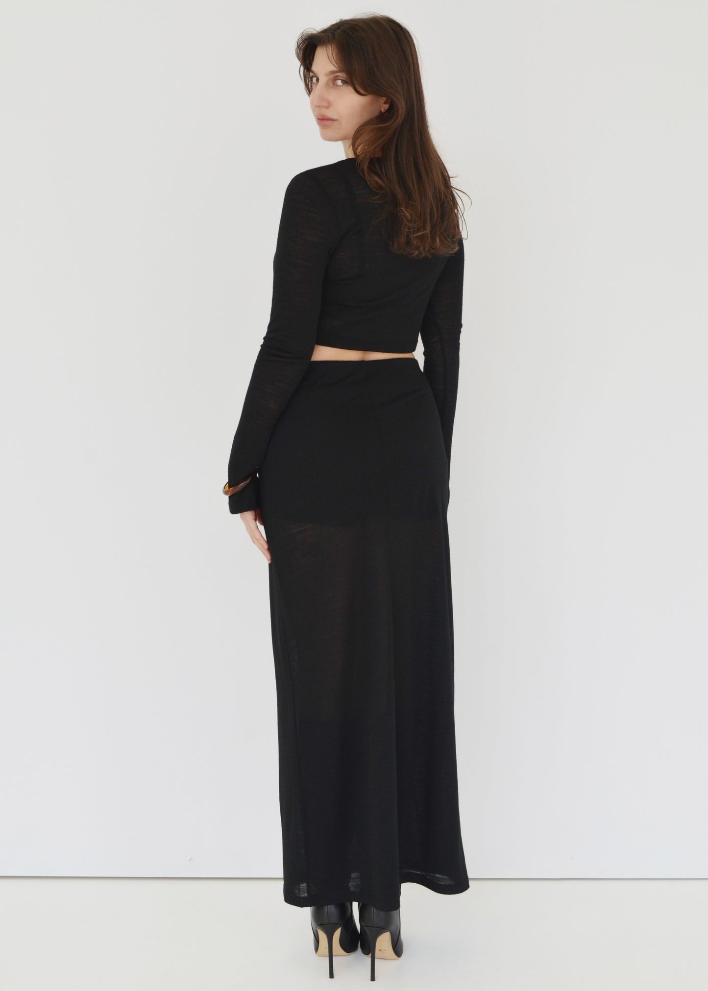 Woman facing the back wearing the Isabel maxi skirt and the matching Tati flared long sleeve crop top in sheer black Japanese Tencel and merino knit. Australian made. 