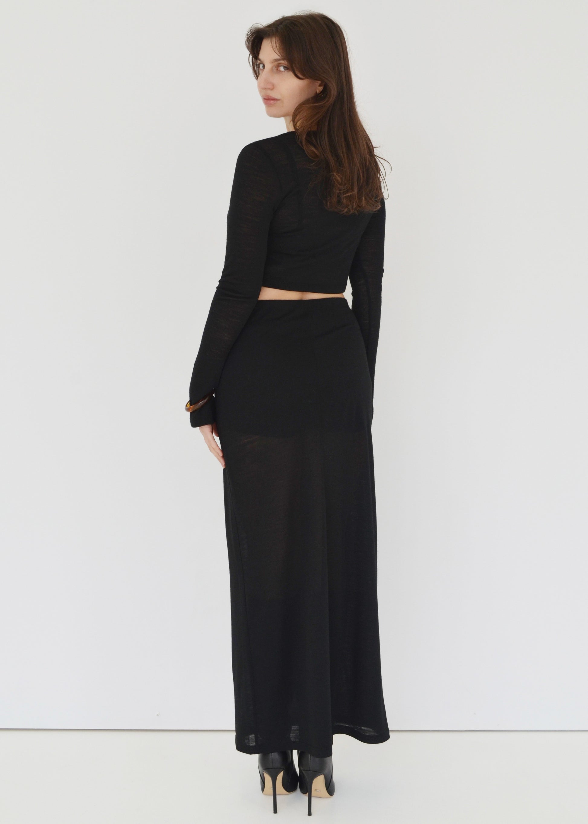 Woman facing the back wearing the Isabel maxi skirt and the matching Tati flared long sleeve crop top in sheer black Japanese Tencel and merino knit. Australian made. 