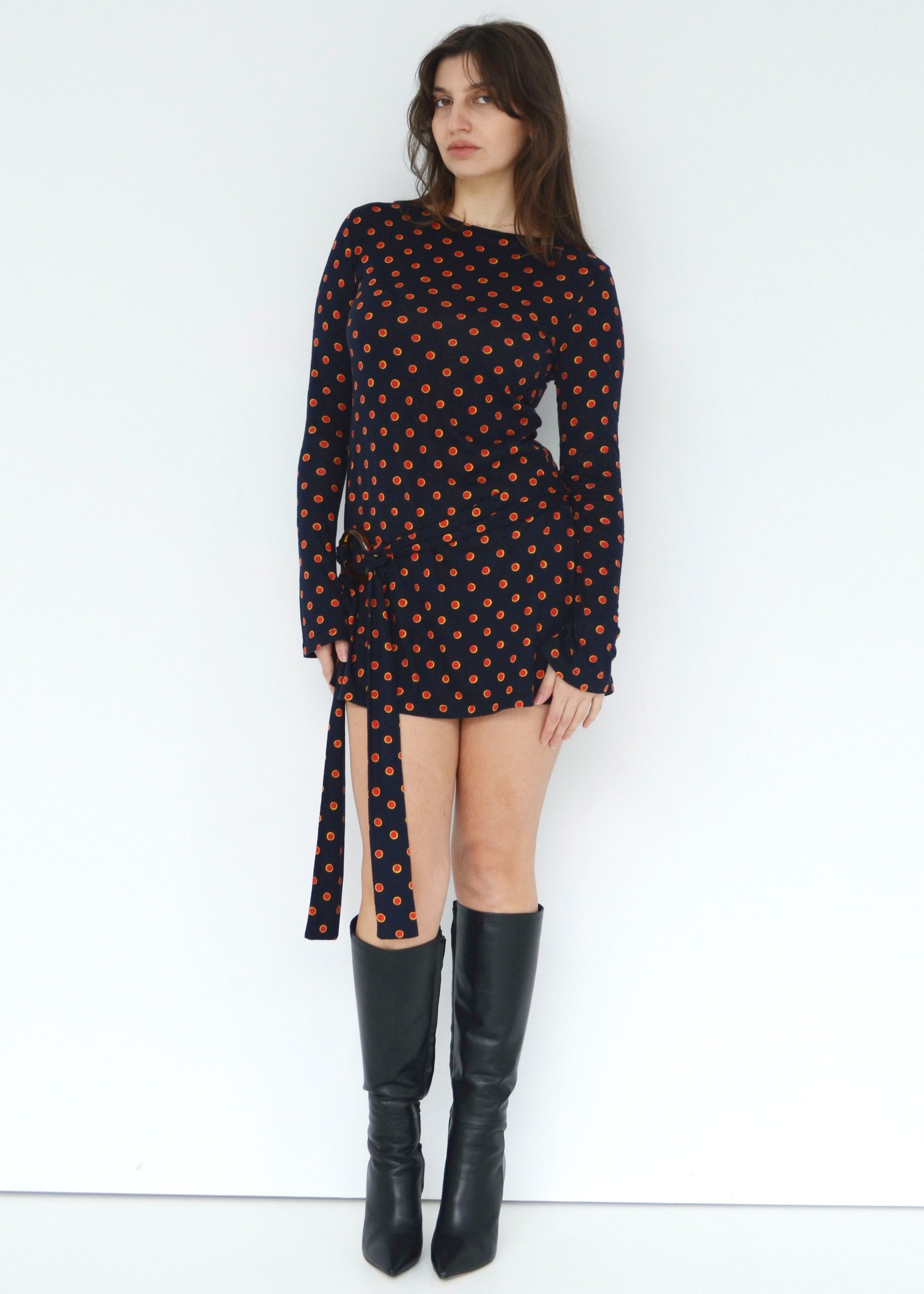 Woman wearing a black dress with red & yellow polka dot and black knee-high boots on a white background