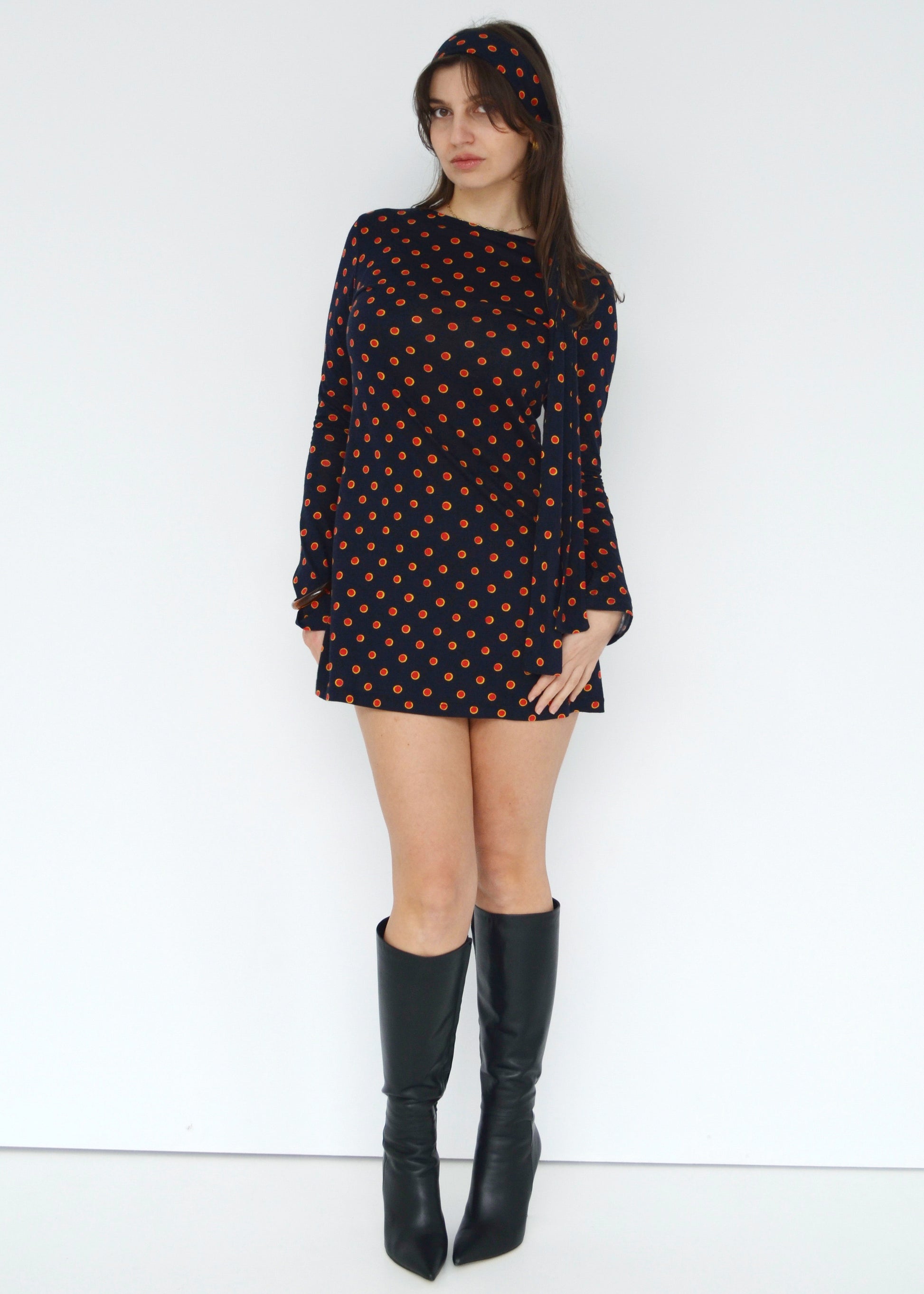 Woman wearing a black dress with red patterns and black knee-high boots on a white background front side