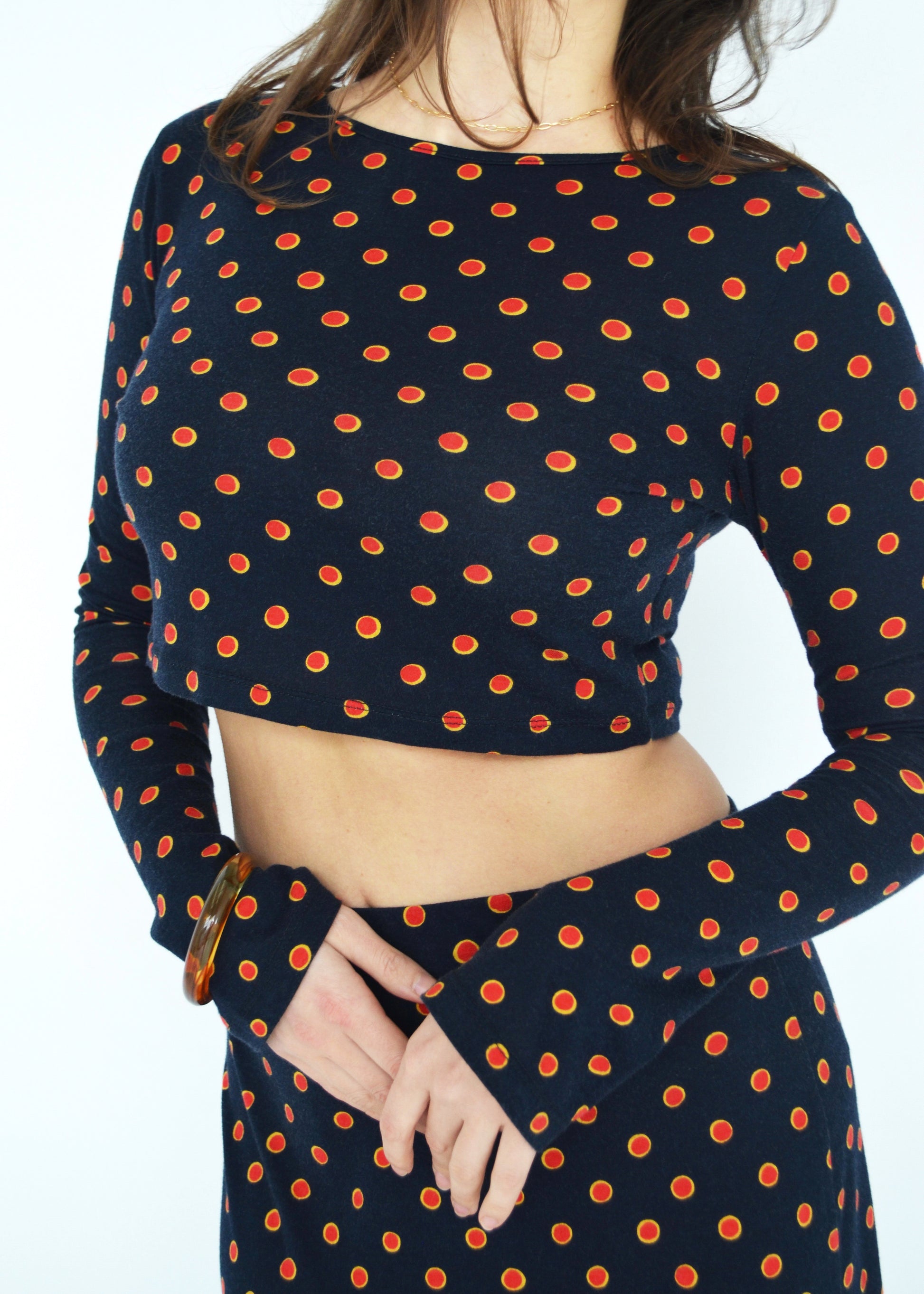 Close up of woman wearing the Isabel maxi skirt and matching Tati flared long sleeve cropped top in navy Japanese Tashi Spot print against white wall. Australian made. 