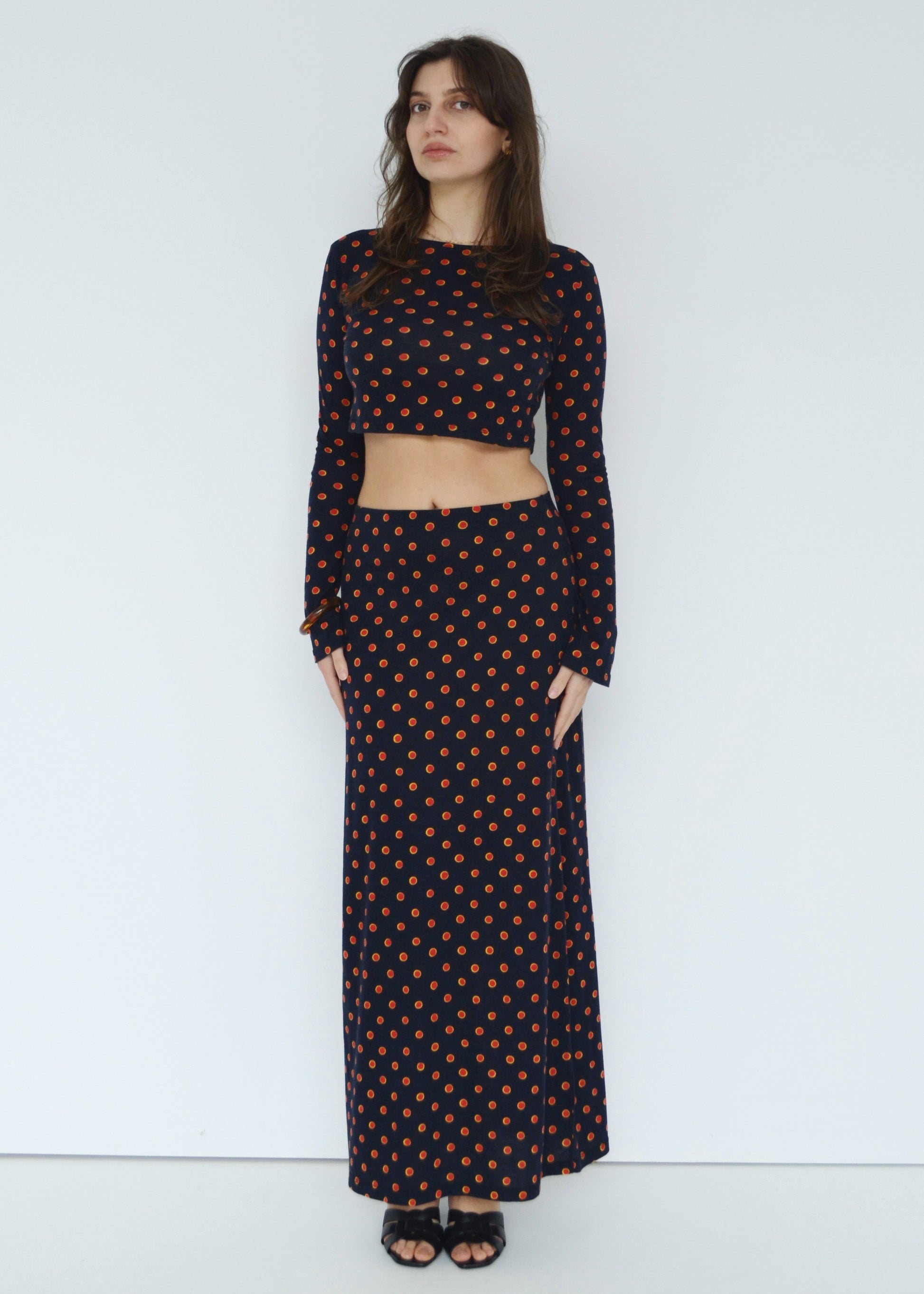 Woman facing front wearing the Isabel maxi skirt low rise and matching Tati flared long sleeve cropped top in navy Japanese Tashi Spot print against white wall. Australian made. 