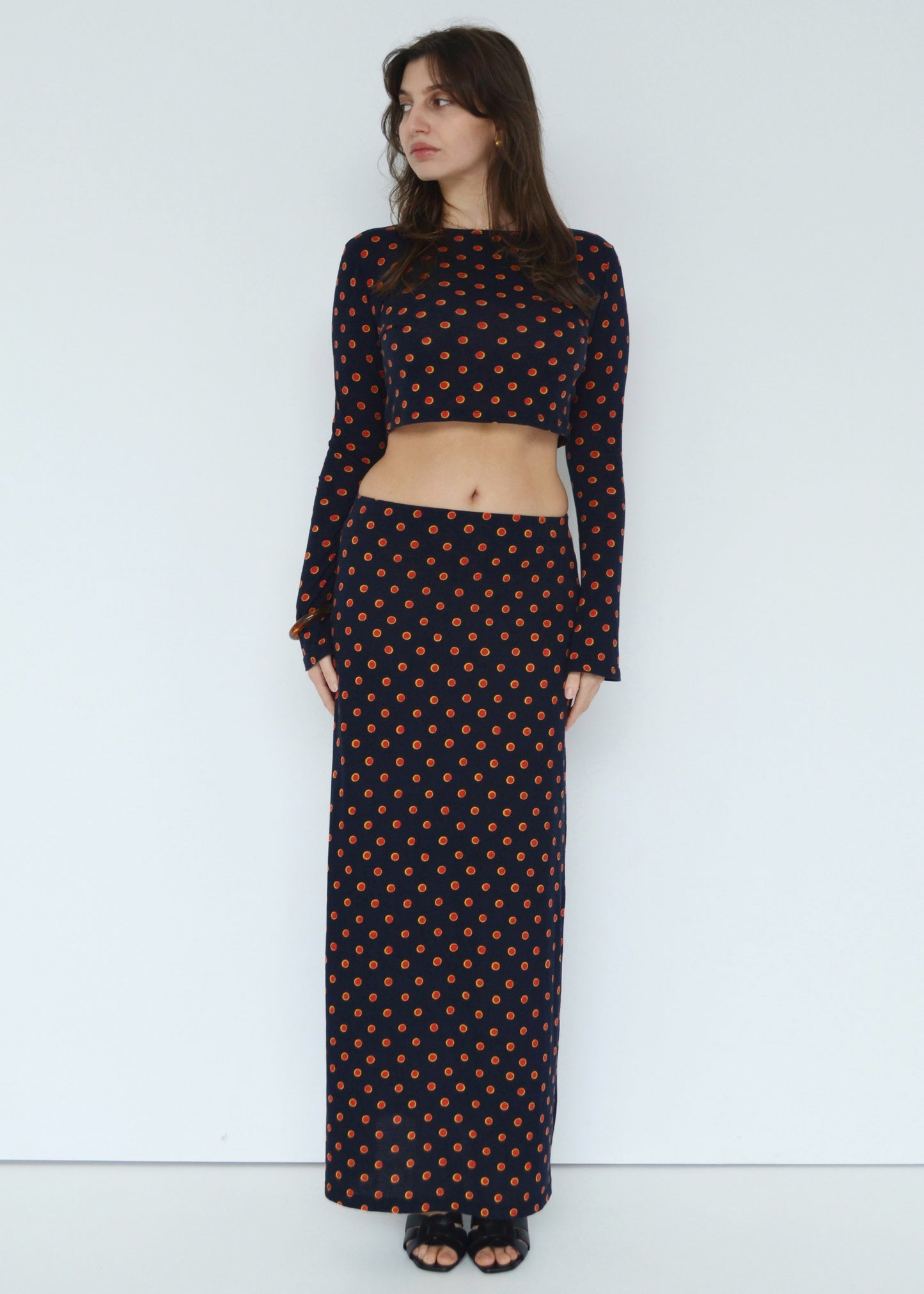 Woman looking to side wearing the Isabel maxi skirt low rise and matching Tati flared long sleeve cropped top in navy Japanese Tashi Spot print against white wall. Australian made. 