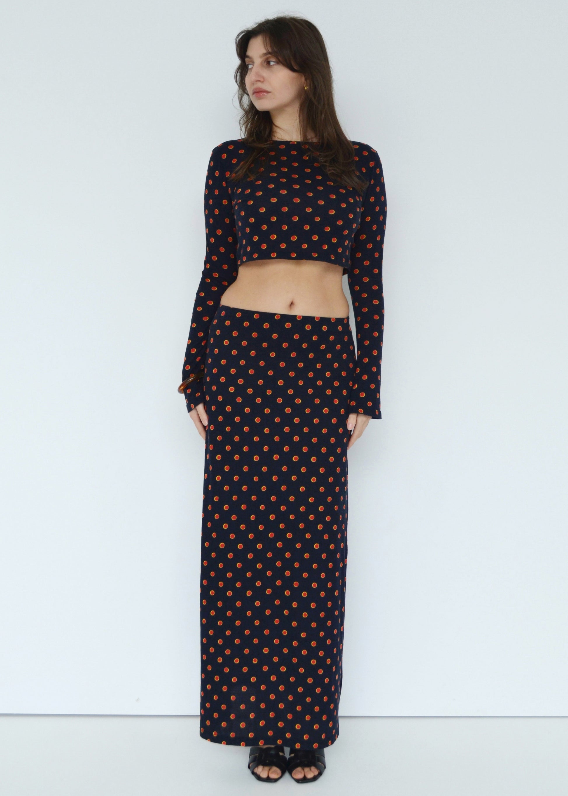 Woman looking to side wearing the Isabel maxi skirt low rise and matching Tati flared long sleeve cropped top in navy Japanese Tashi Spot print against white wall. Australian made. 