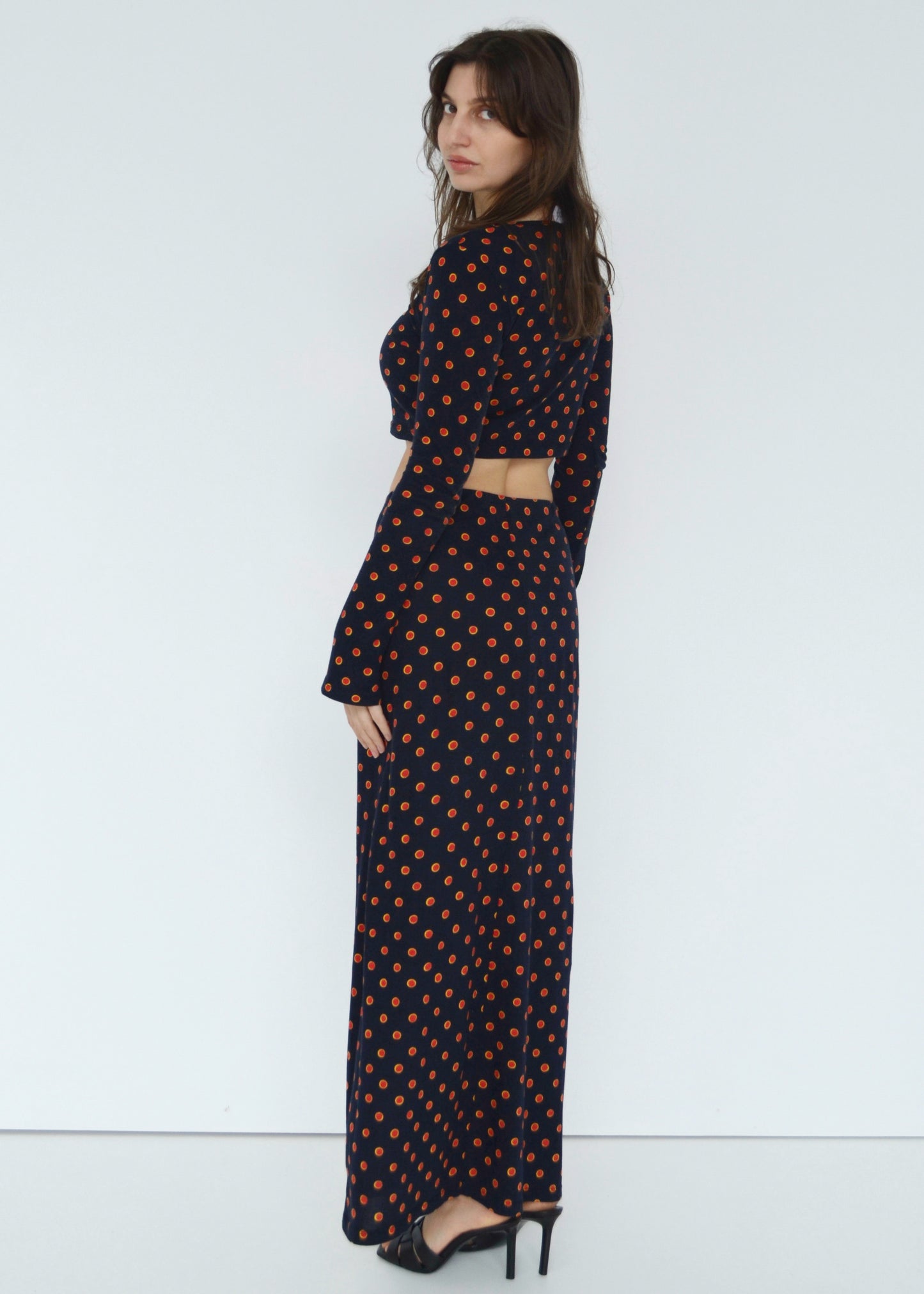 Woman facing slightly on towards their side wearing the Isabel maxi skirt low rise and matching Tati flared long sleeve cropped top in navy Japanese Tashi Spot print against white wall. Australian made. 