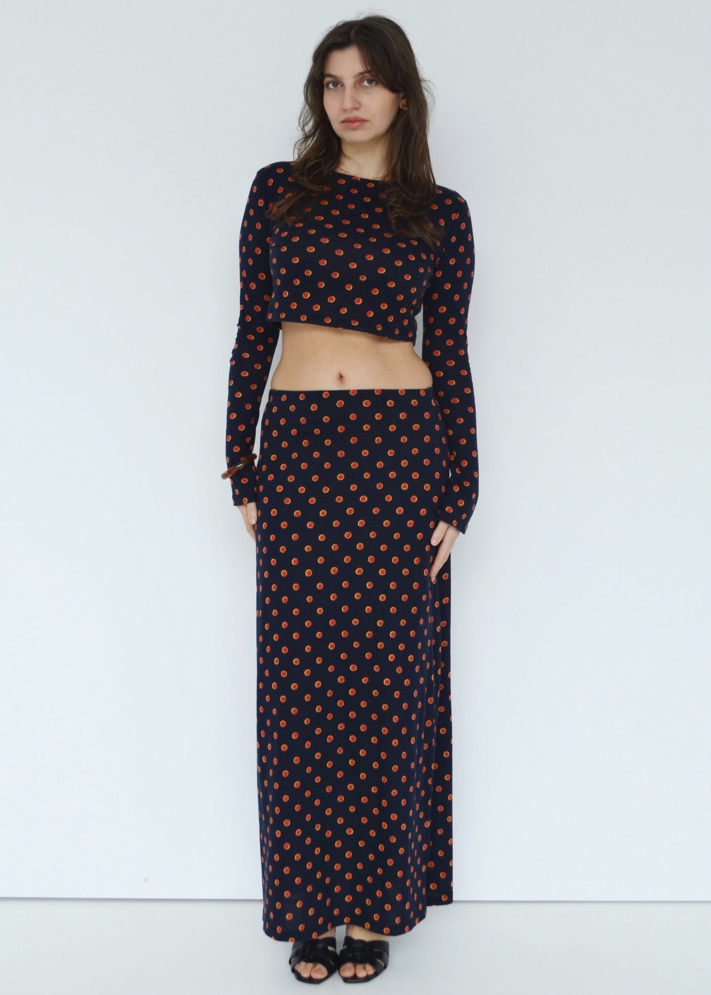 Woman facing front wearing the Isabel maxi skirt low rise and matching Tati flared long sleeve cropped top in navy Japanese Tashi Spot print against white wall. Australian made. 