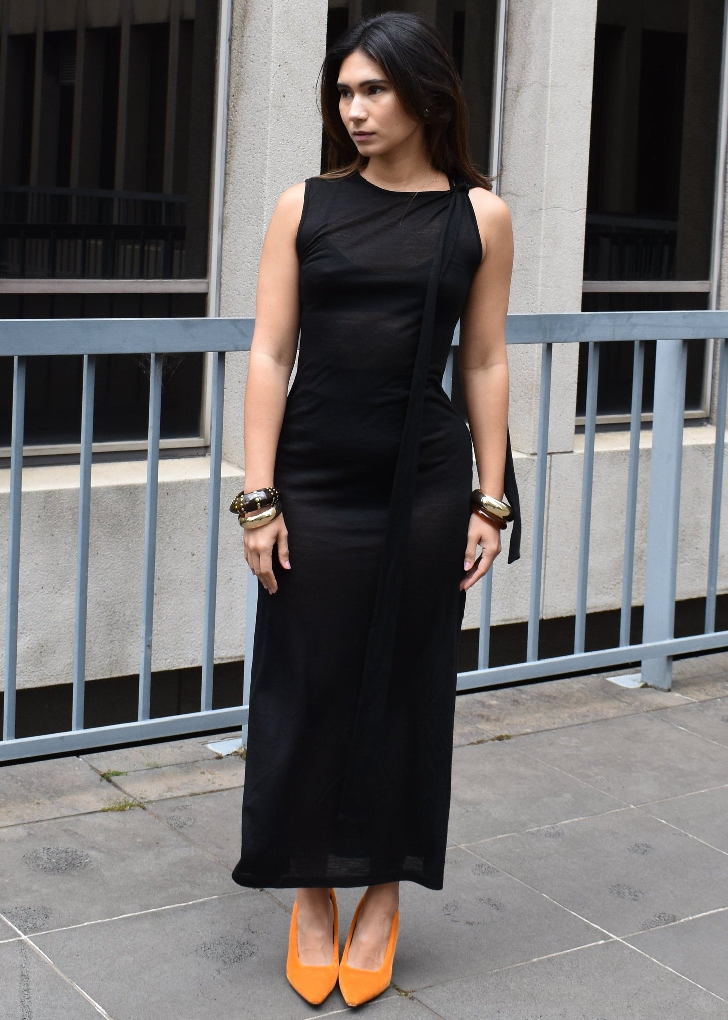 Woman in a black dress with orange shoes standing in front of a building.

