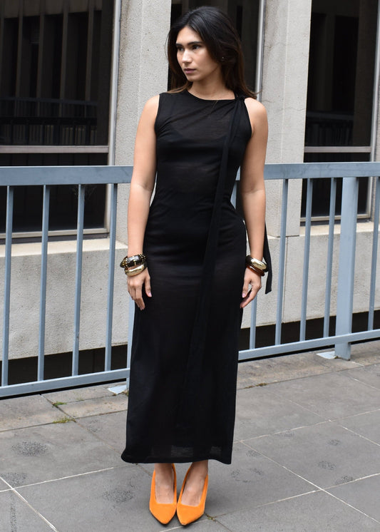 Woman in a black dress with orange shoes standing in front of a building.

