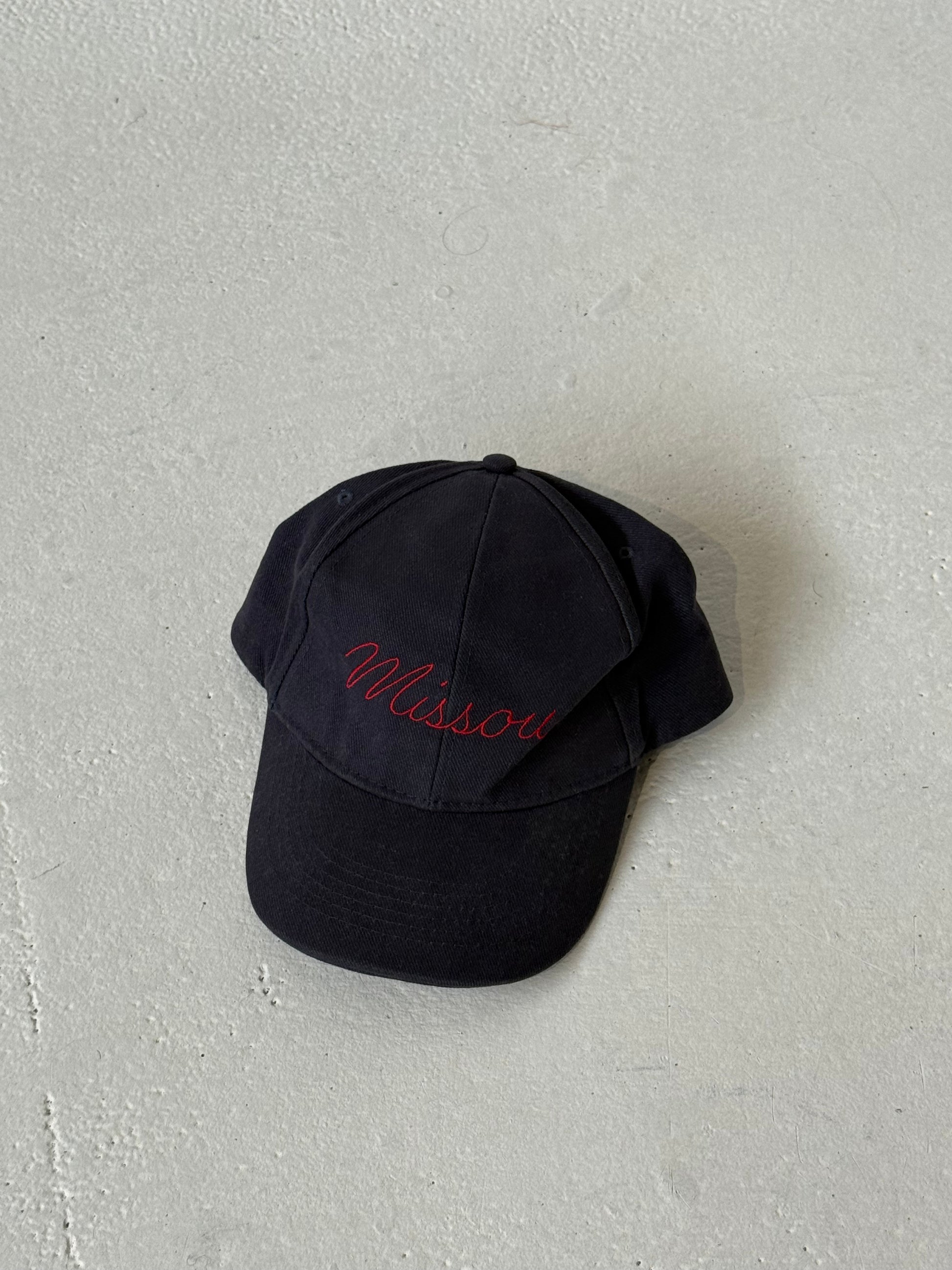 The Missou cap in navy cotton with red embroidered cursive logo on stone floor. 