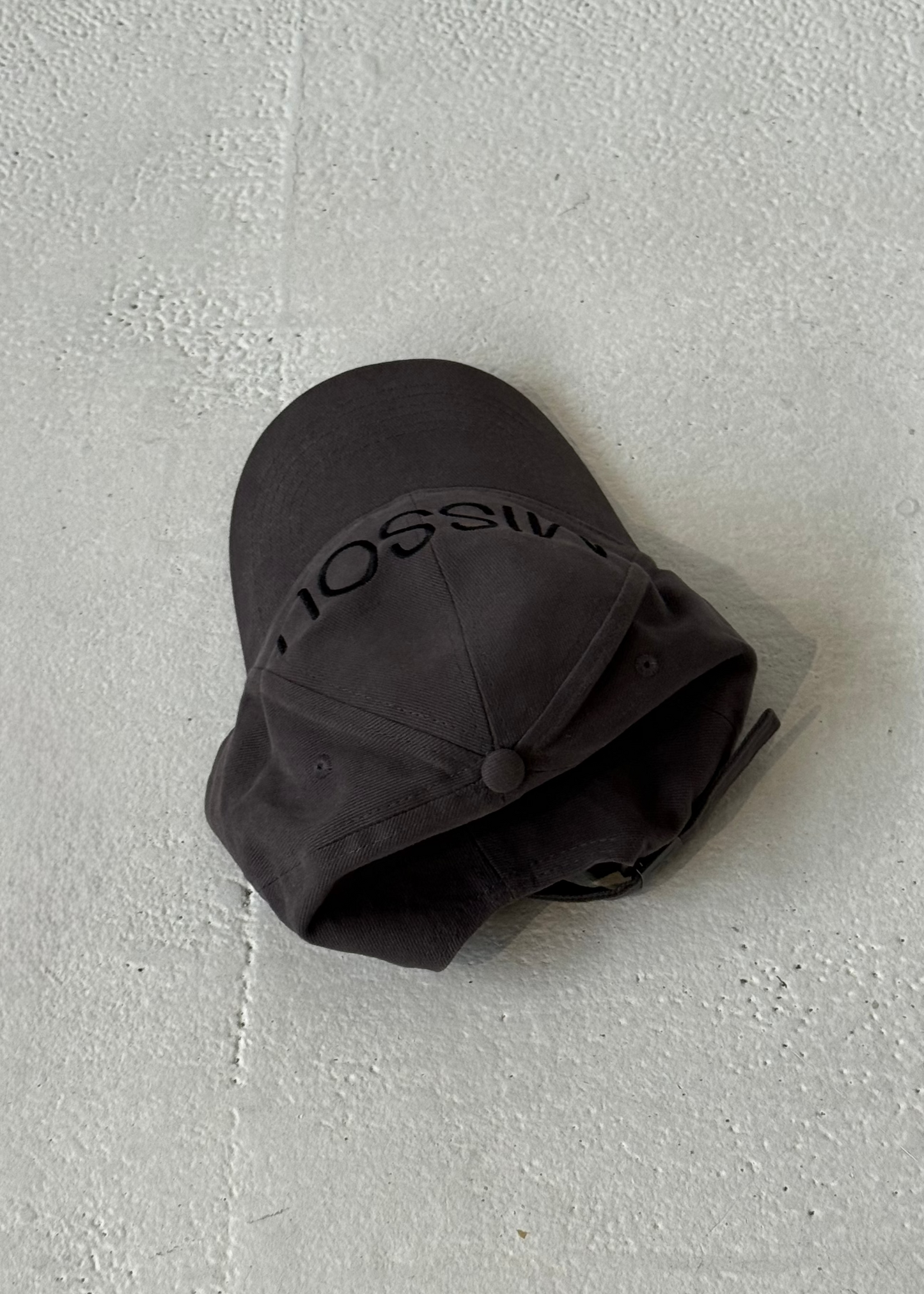 Back of the Missou cap in charcoal grey cotton with embroidered block logo on a stone floor. 
