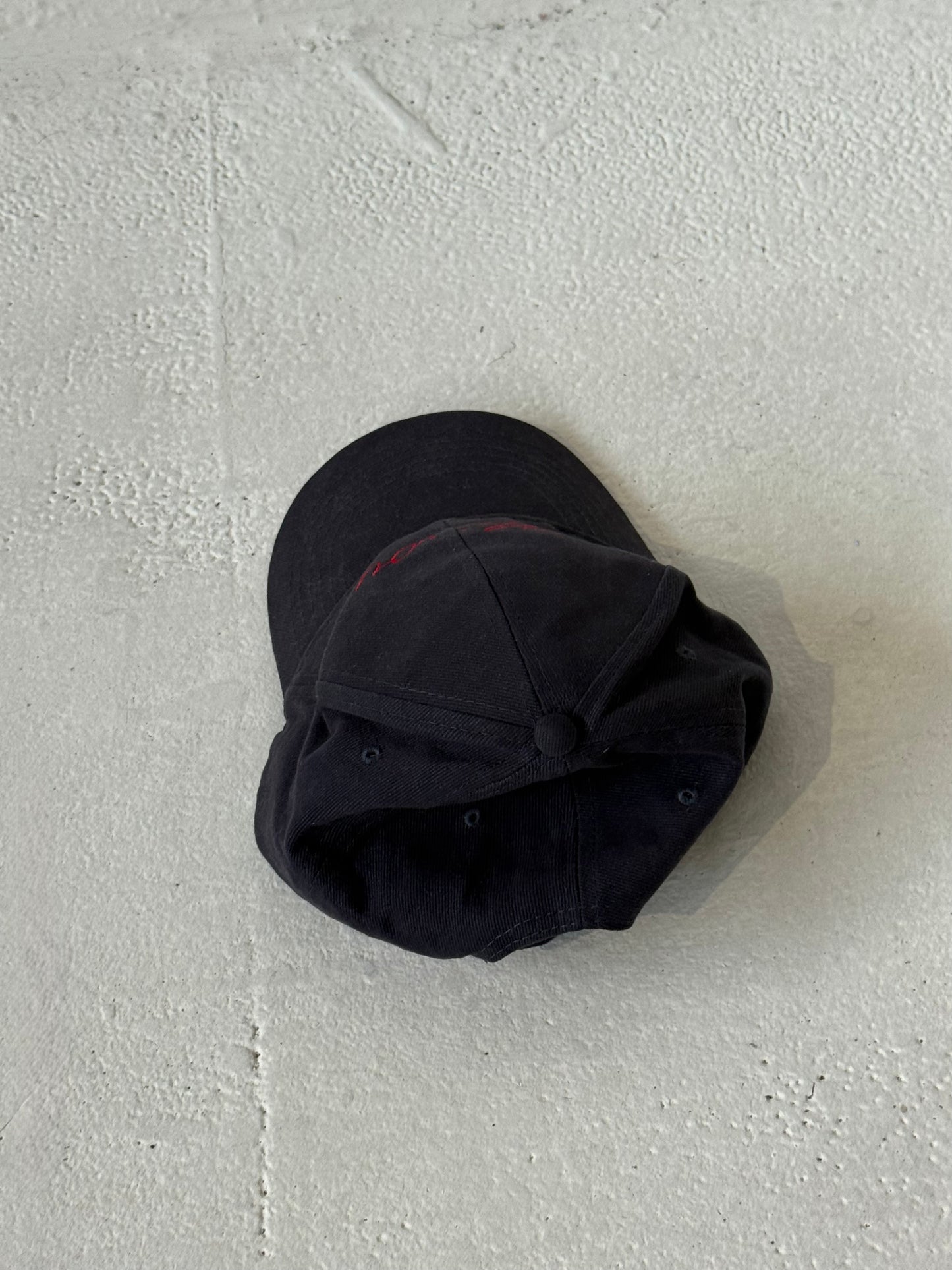 Back of the Missou cap in navy cotton with red embroidered cursive logo on stone floor. 