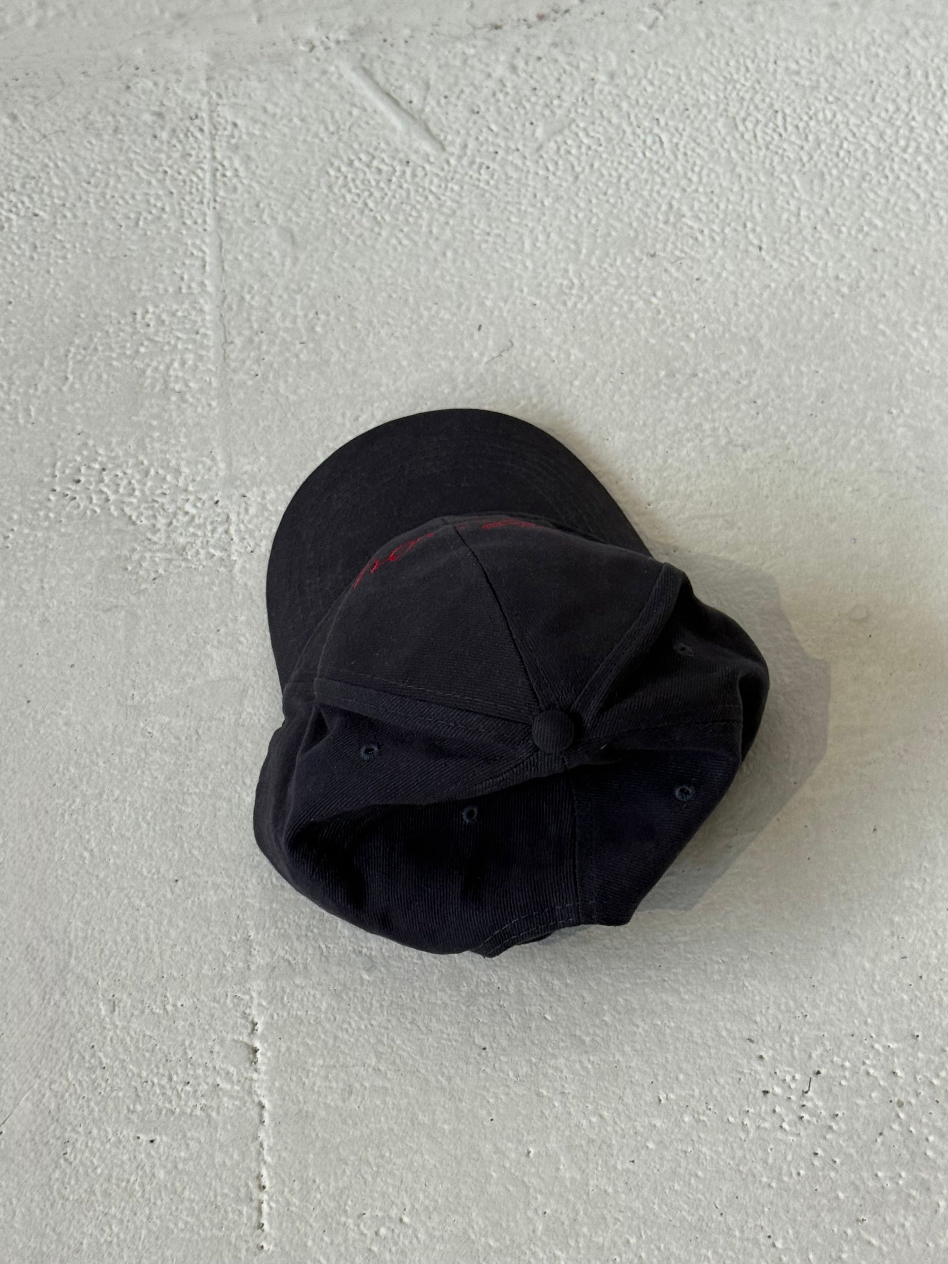 Back of the Missou cap in navy cotton with red embroidered cursive logo on stone floor. 