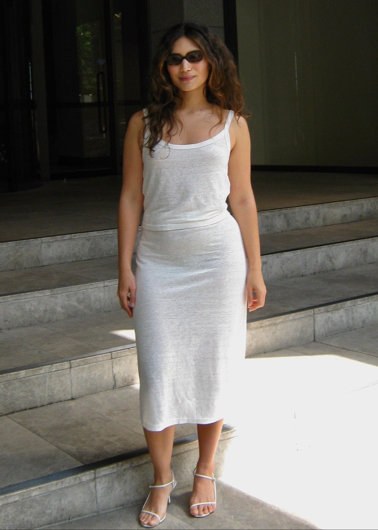 Woman in a white Japanese linen cami and midi skirt standing on steps in an urban setting

