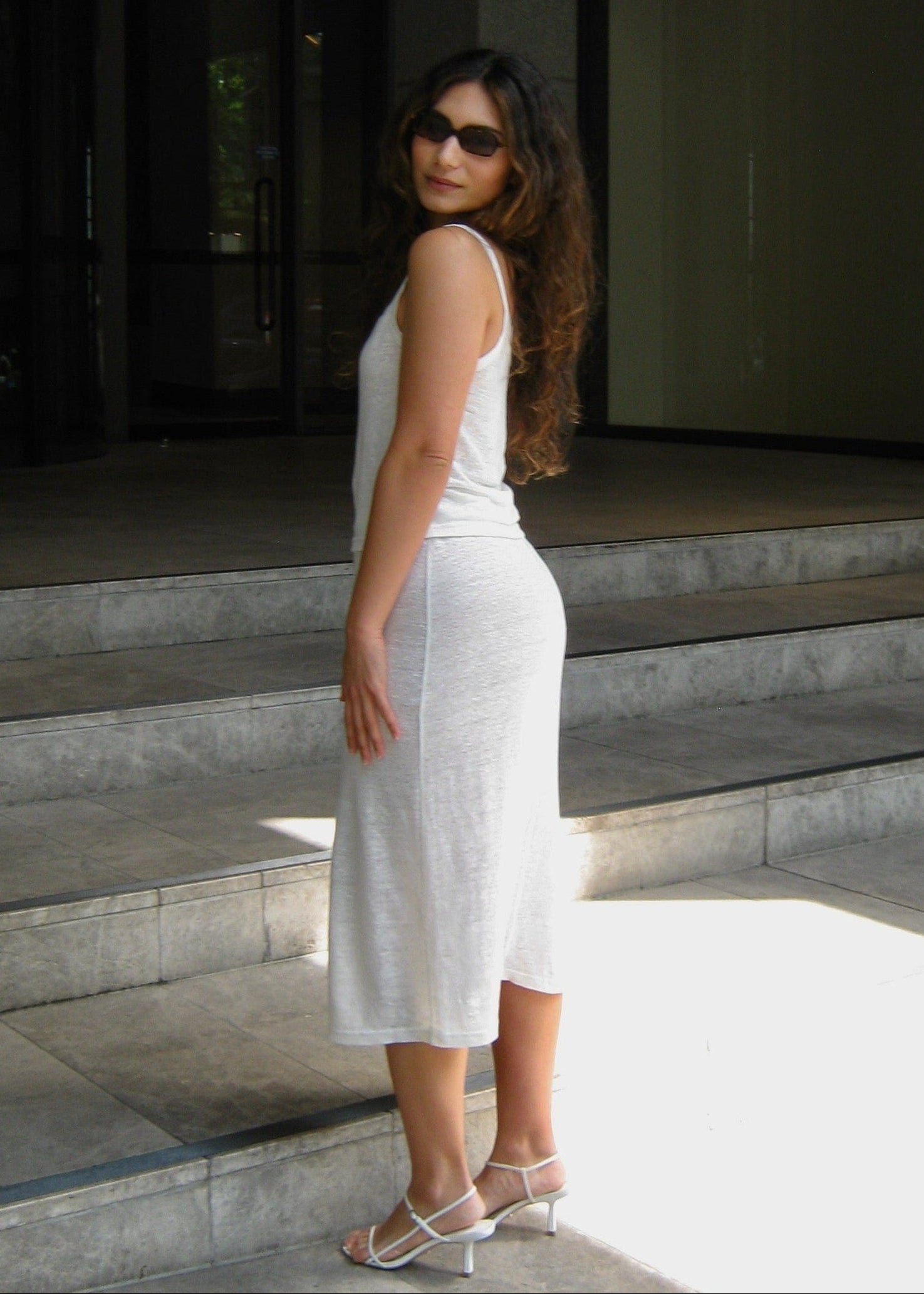 Woman in a white Japanese linen cami top and midi skirt standing on steps outside a modern building

