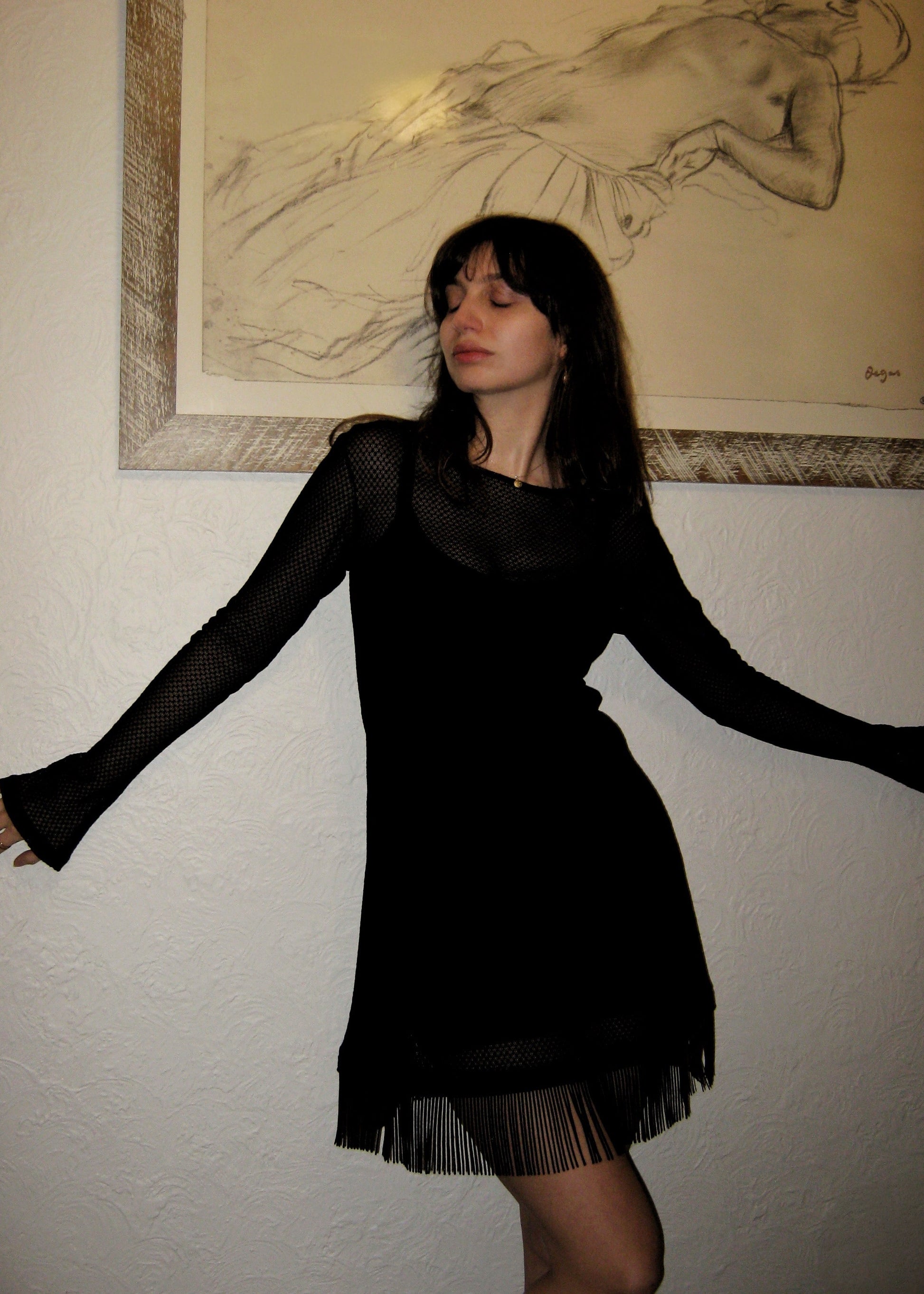 Woman wearing the Kea micro mini dress with fringe edge in black Italian micro floral lace leaning against the wall. Made in Australia.