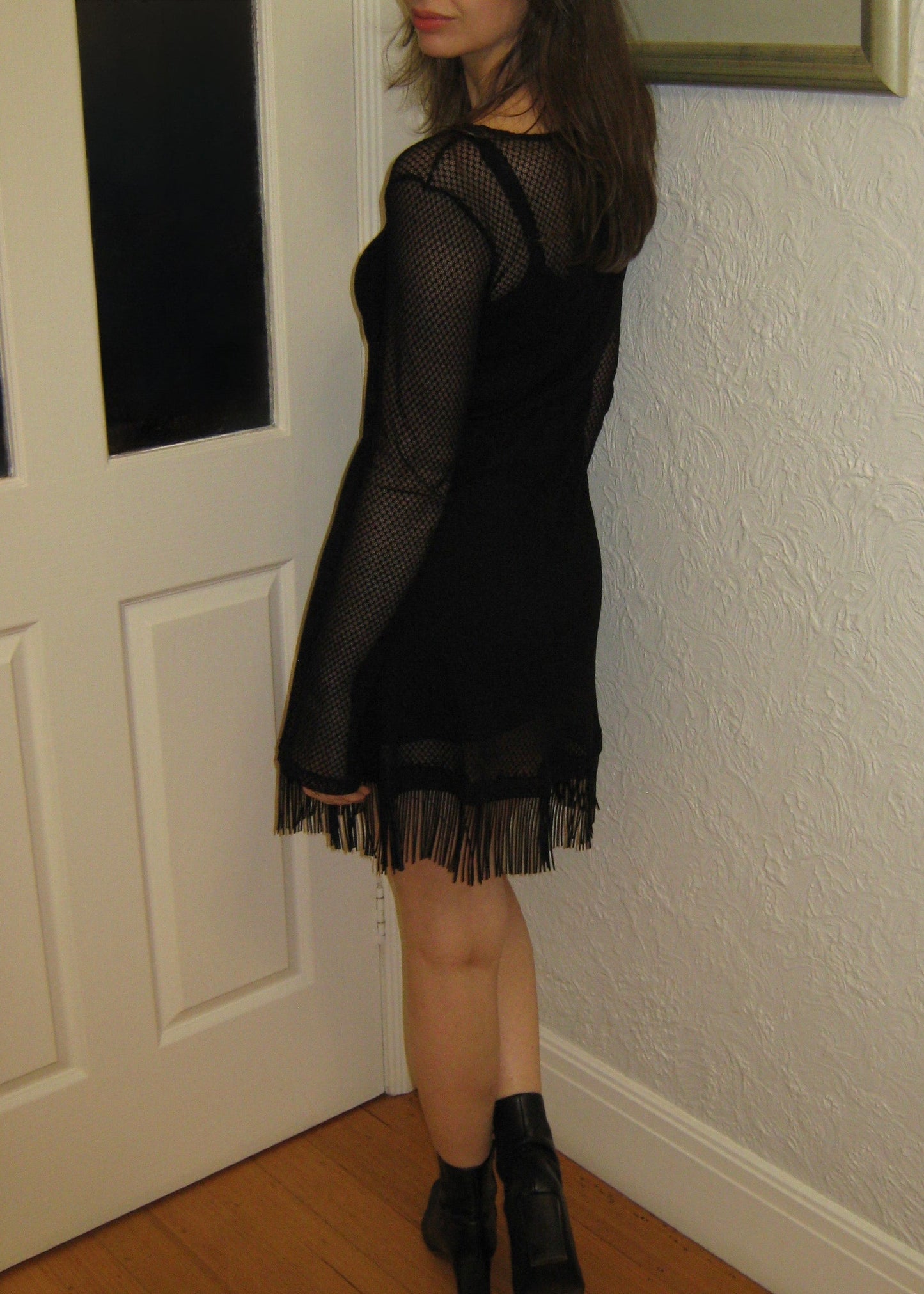 Woman wearing the Kea micro mini dress with fringe edge in black Italian micro floral lace facing the wall. Made in Australia.